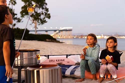 kids eating roasted marshmellows using a Solo Stove at the beach