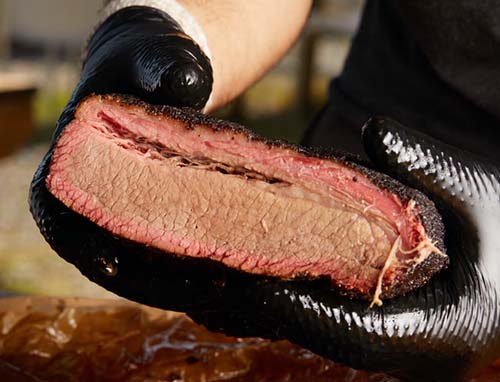 man wearing gloves and holding a brisket