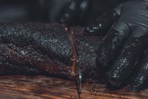 person cutting a smoked brisket