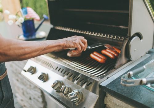 Man Grills Sausages on an Outdoor Grill