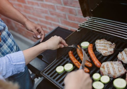 Two People Grilling Meat, Sausages and veggies