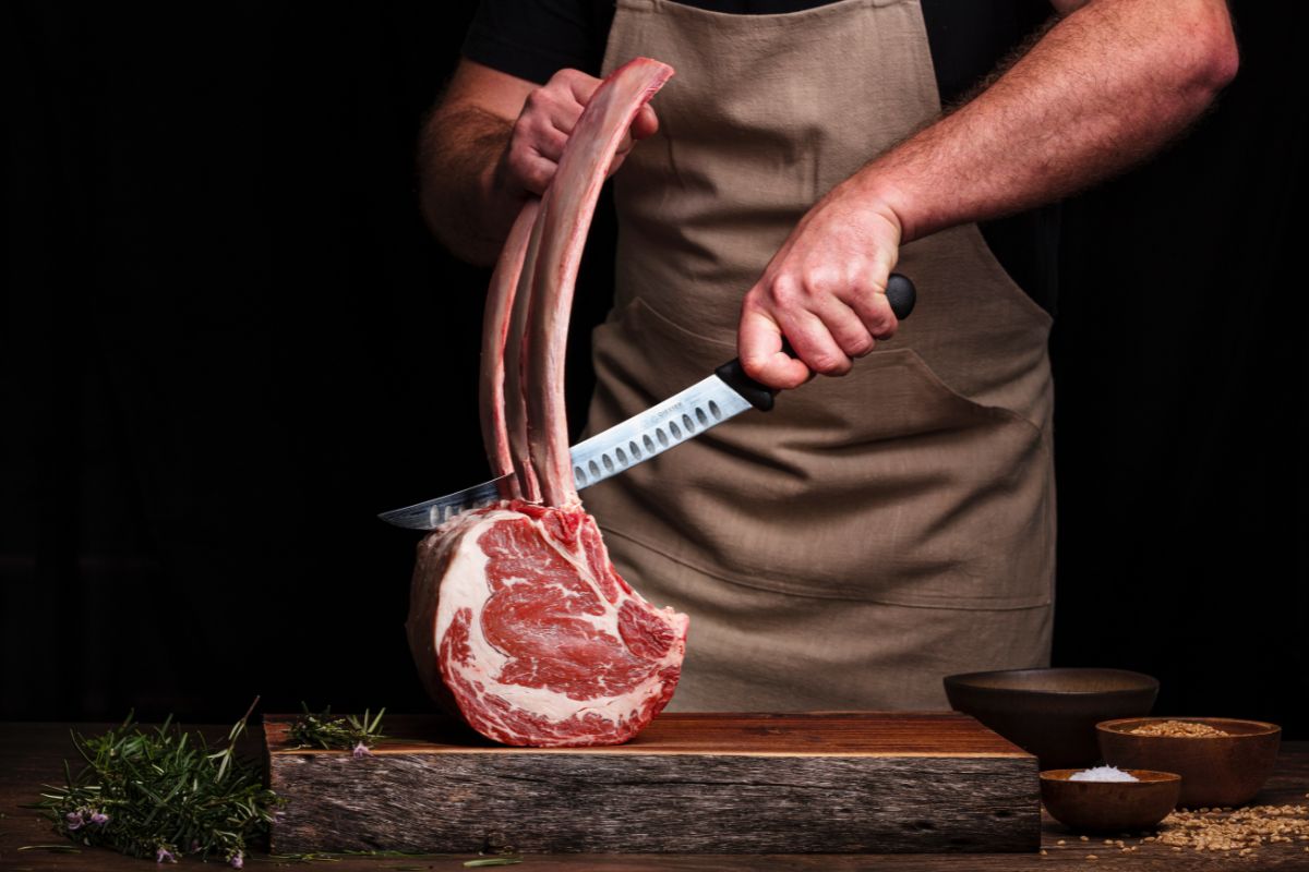 Person Wearing an Apron Cutting a Boned Meat with a Sharp Knife