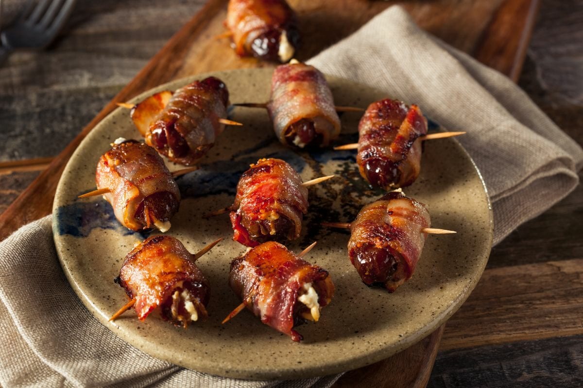 Bacon Wrapped Smoked Pig Shots Lined up on a Ceramic Plate