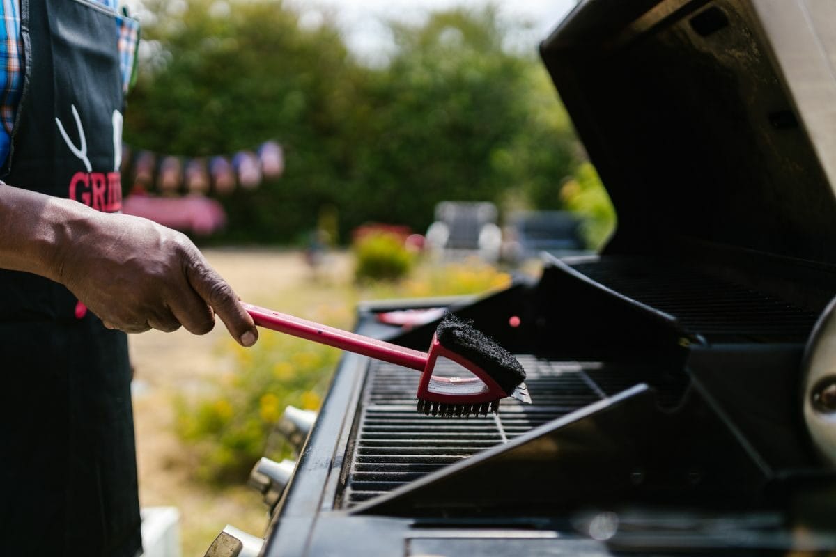 Man Wearing a Black Apron Cleaning a Grill with a Wired Brush