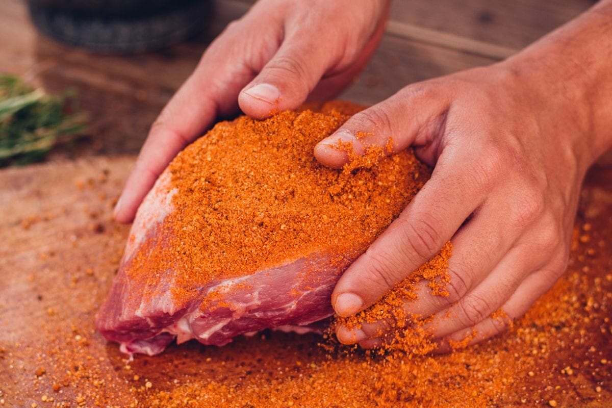 Person Rubbing Dry Seasoning into a Piece of Pork
