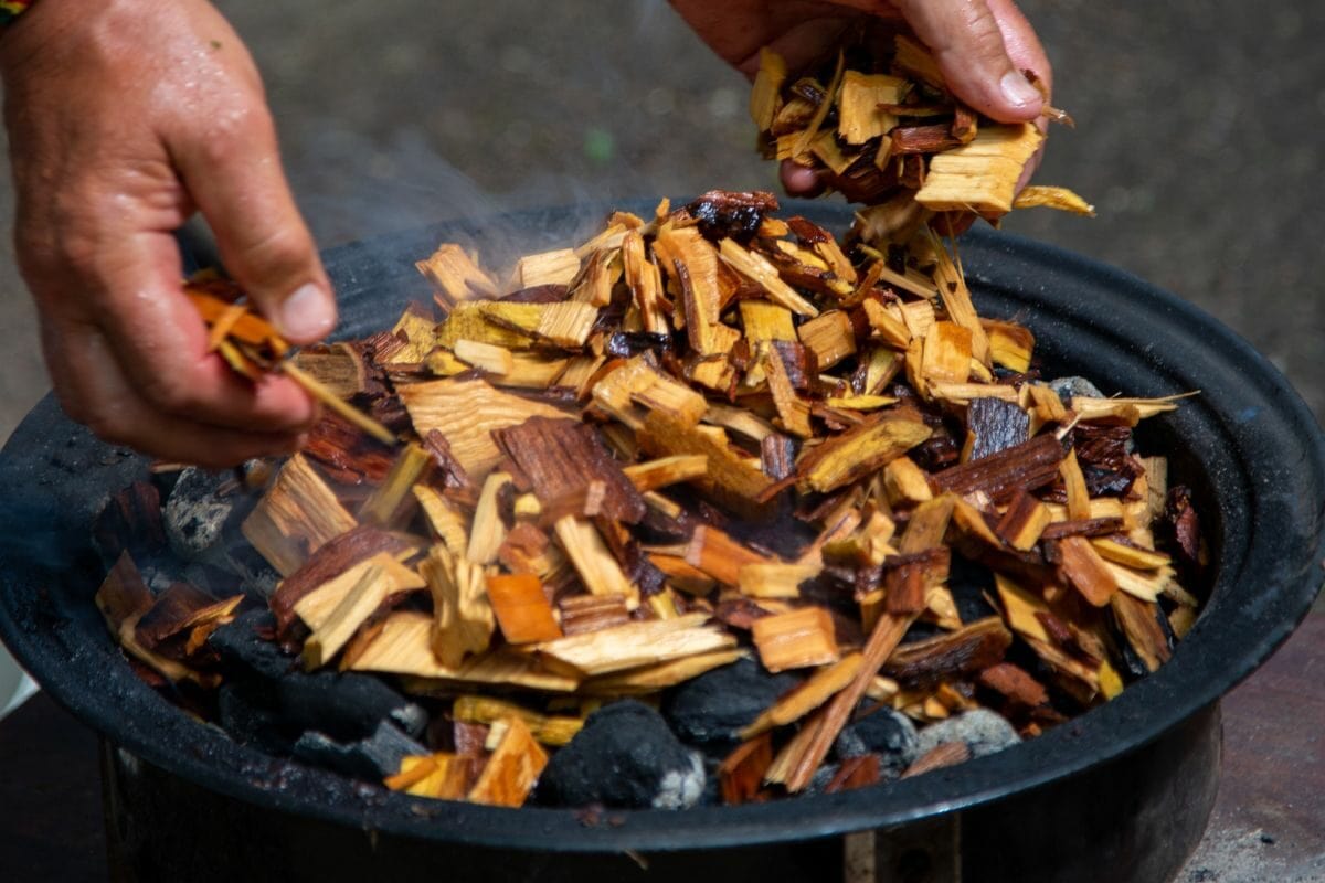 Person Adding Soaked Wood Chips and Charcoal in a Grill