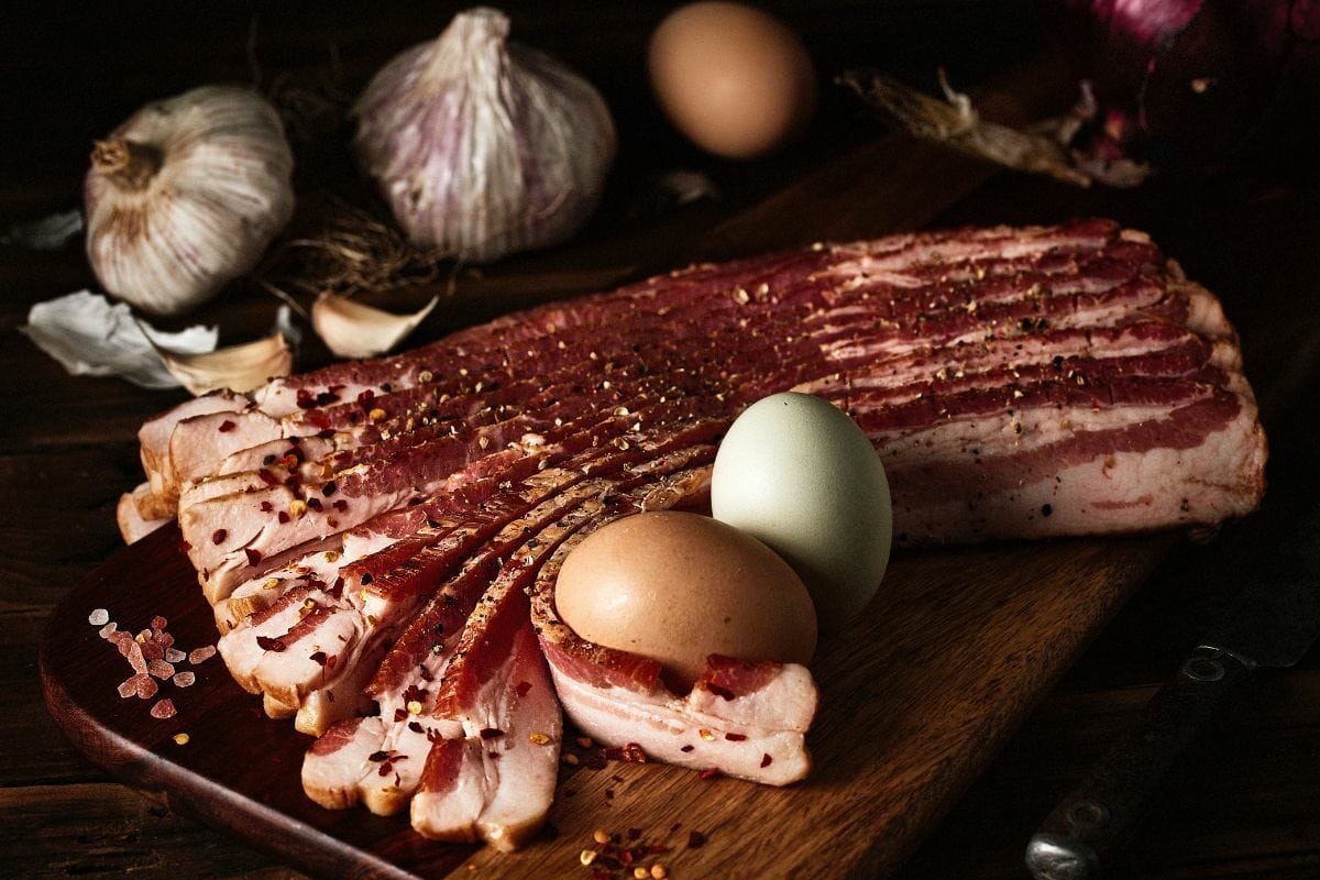 freshly sliced smoked bacon with two eggs, garlic and onion